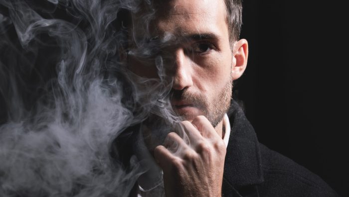 Face, fashion and smoke with a man portrait in studio on a dark background for trendy style. Cloud,.