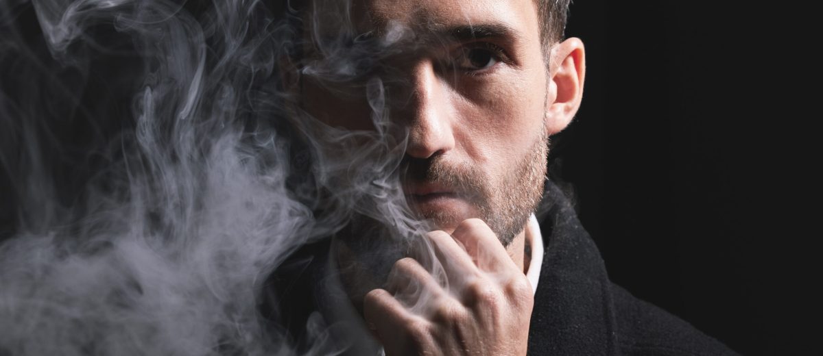 Face, fashion and smoke with a man portrait in studio on a dark background for trendy style. Cloud,.