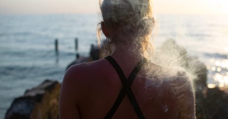 A female smoking a joint shot from behind with a blurred sea in the background