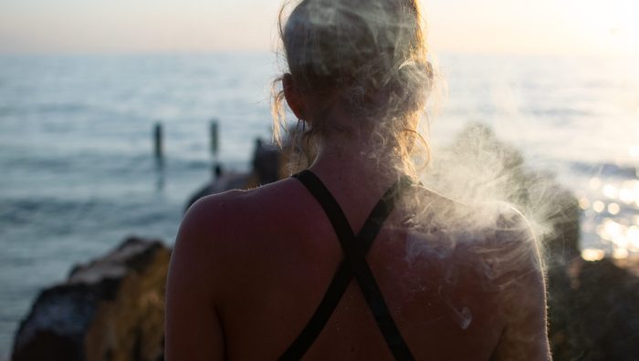 A female smoking a joint shot from behind with a blurred sea in the background