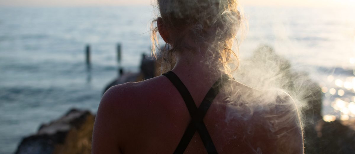 A female smoking a joint shot from behind with a blurred sea in the background